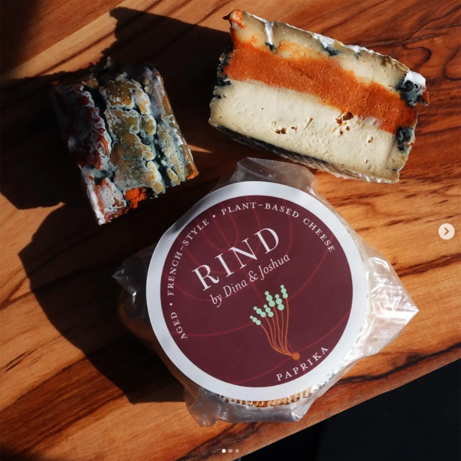 vegan bleu cheese wheel cross hair and container of vegan paprika dip on a wood serving board