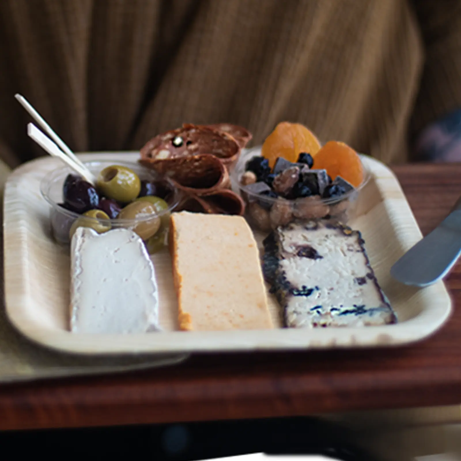 Plant-based cheese plate with a slice of cashew brie, cashew smoked cheddar, and soy based bleu cheese accompanied by vegan koji salami, dried fruit, nuts and olives.