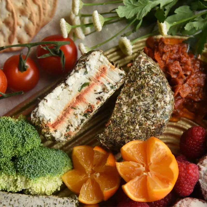 vegan plant based tomato fromage, crusted with herbs and surrounded by vegetables and fruits