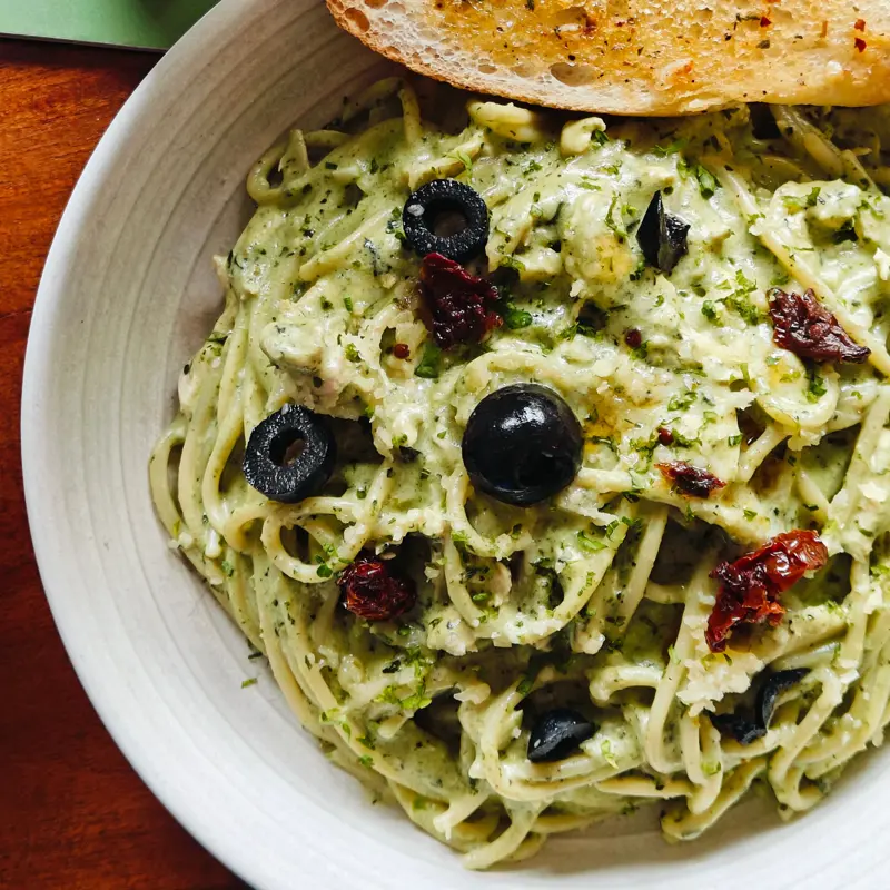 bowl of pasta with green sauce and olives with parmesan
