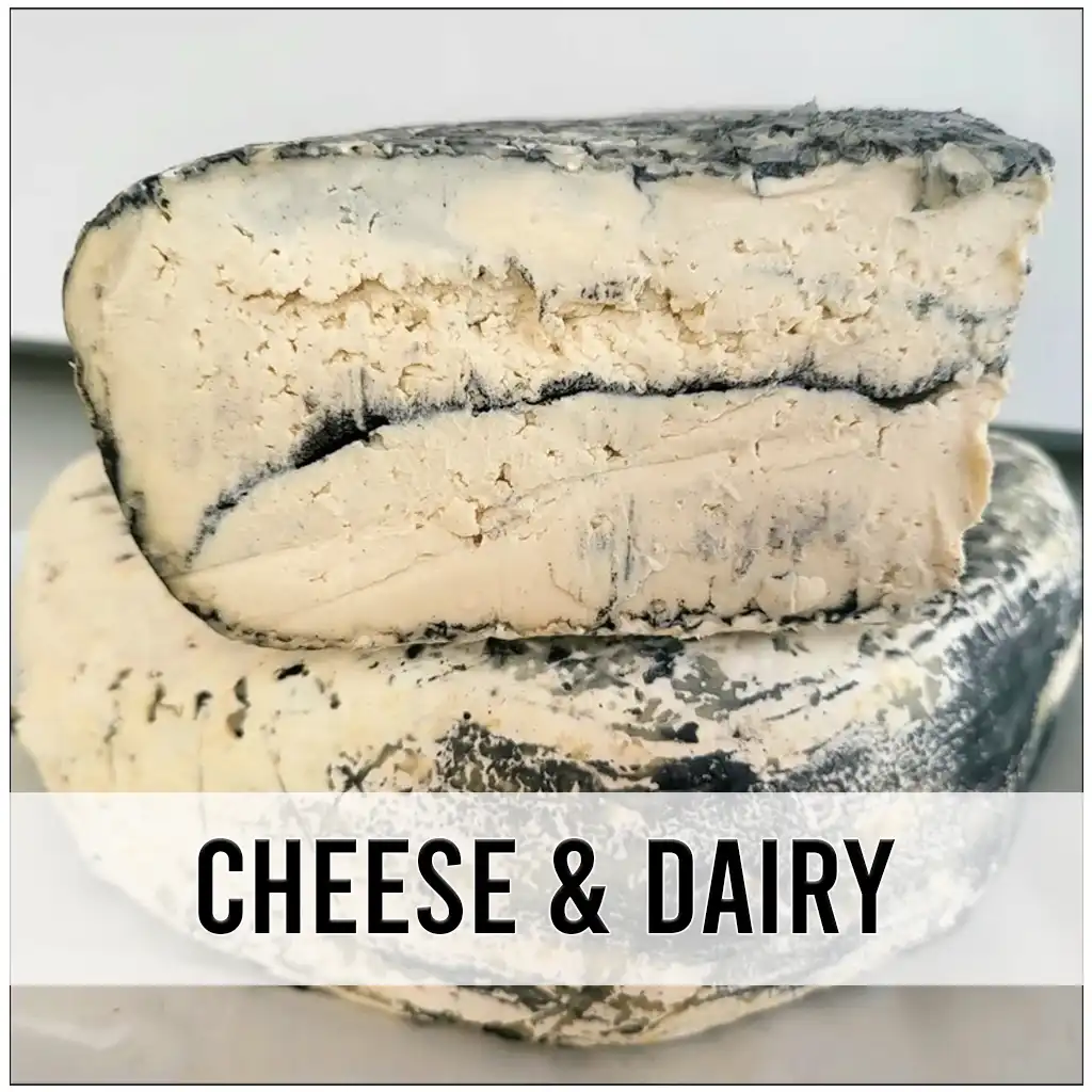 two vegan brie cheese wedges with an ash rind stacked on top of each other, the one on top is sliced.