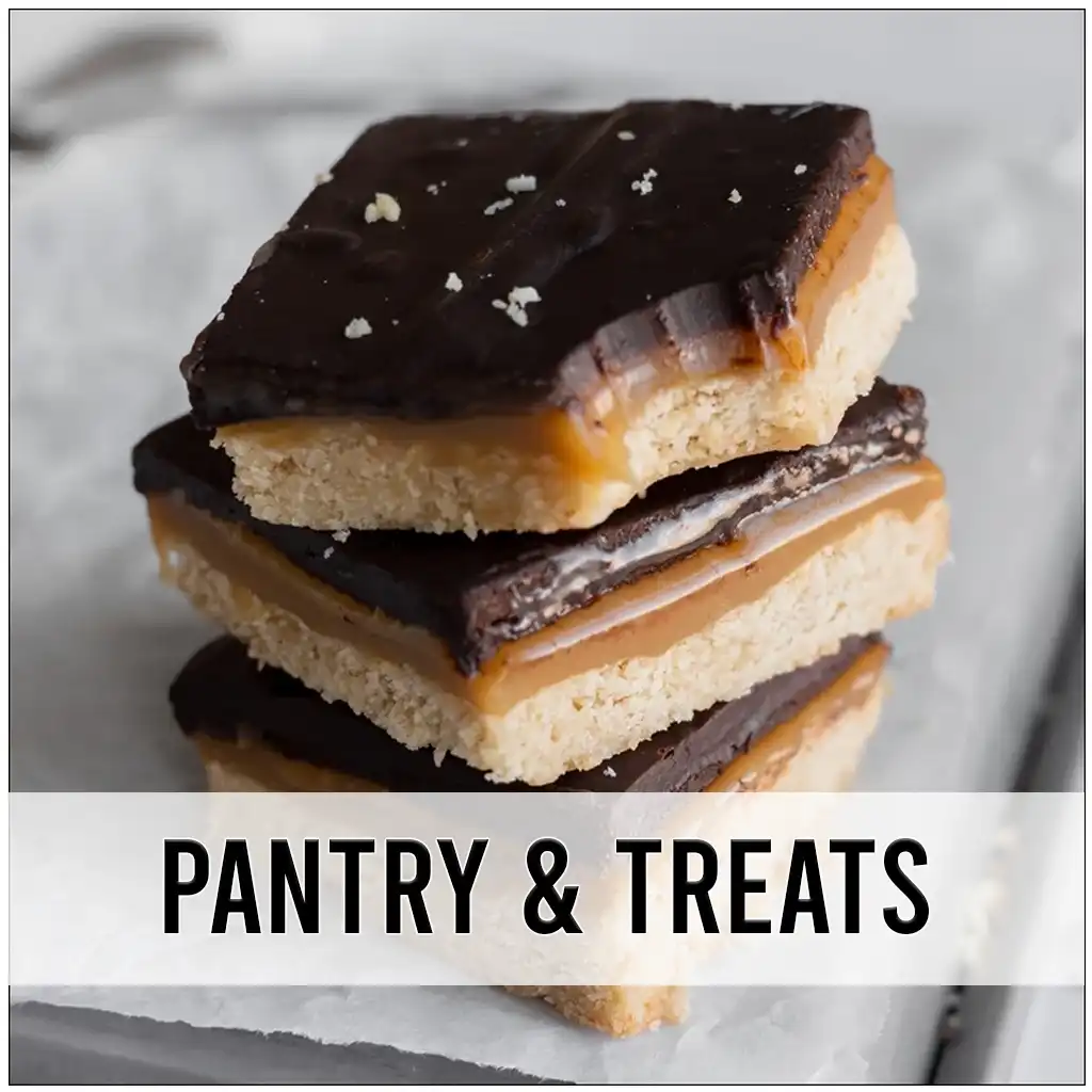 3 chocolate and caramel millionaire bars stacked on top of parchment paper. One has a bite taken out of it.