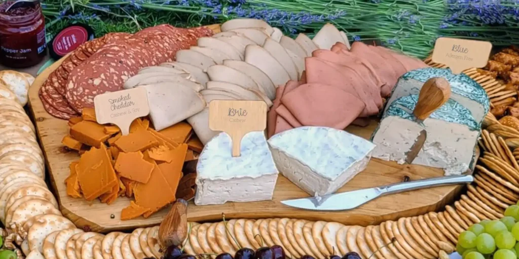 Vegan charcuterie board with salami, turkey, ham, smoked cheddar, vegan brie and vegan blue surrounded by crackers and fruit