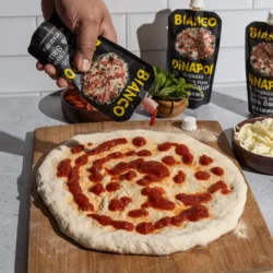 organic new york style pizza sauce being put onto a pizza crust