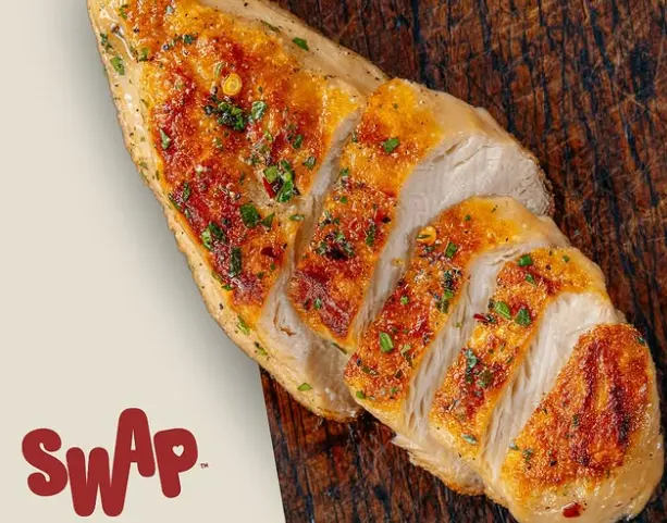 A close-up shot of a crispy, golden vegan flatbread fresh out of the oven, generously layered with creamy pesto cream cheese, savory seared plant-based chicken shreds, and vibrant julienned sun-dried tomatoes.