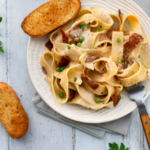 Pasta and salami on a plate with cream sauce and bread