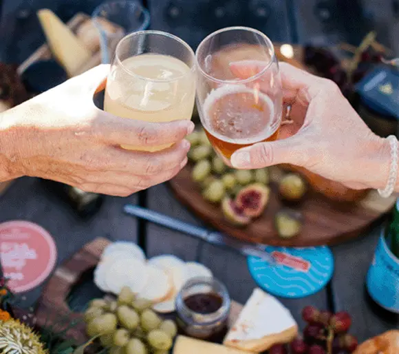 Two hands clinking glasses over a cheese board